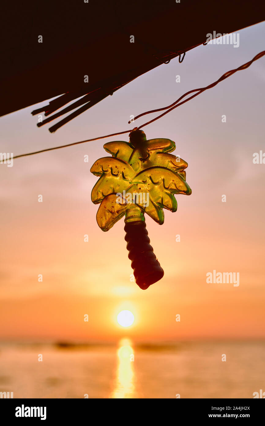 Palm tree shaped festive string light decorating a rustic beach bar cafe with a sunset sea sky beach background - tropical beach holiday symbol Stock Photo