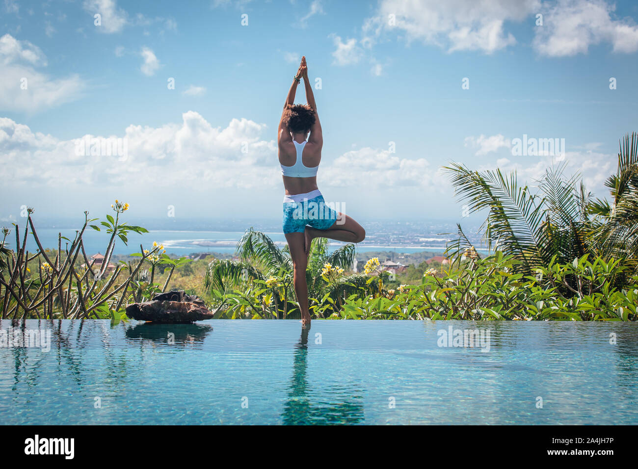 Young woman practicing yoga pose asana on the edge of infinity pool with breathtaking view at the villa in Bali Stock Photo