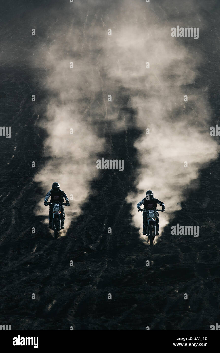 Two friends racing on custom retro style cafe racer black motorcycles on the black lava sand at sunrise on mount Batur, Bali, Indonesia Stock Photo