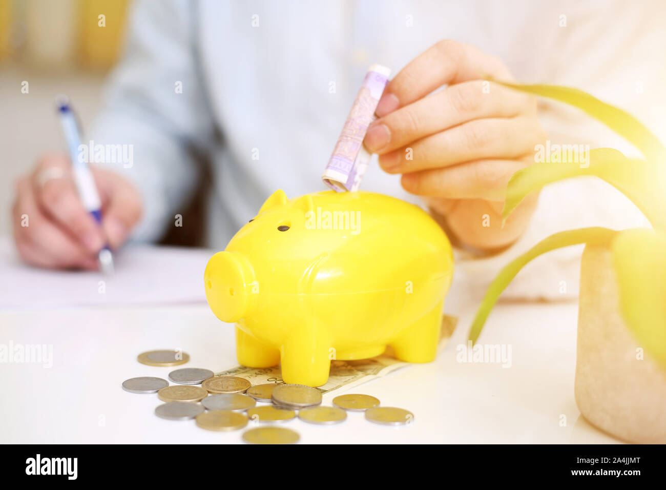 Picture of person depositing money in a yellow piggy bank. Isolated on background. Stock Photo