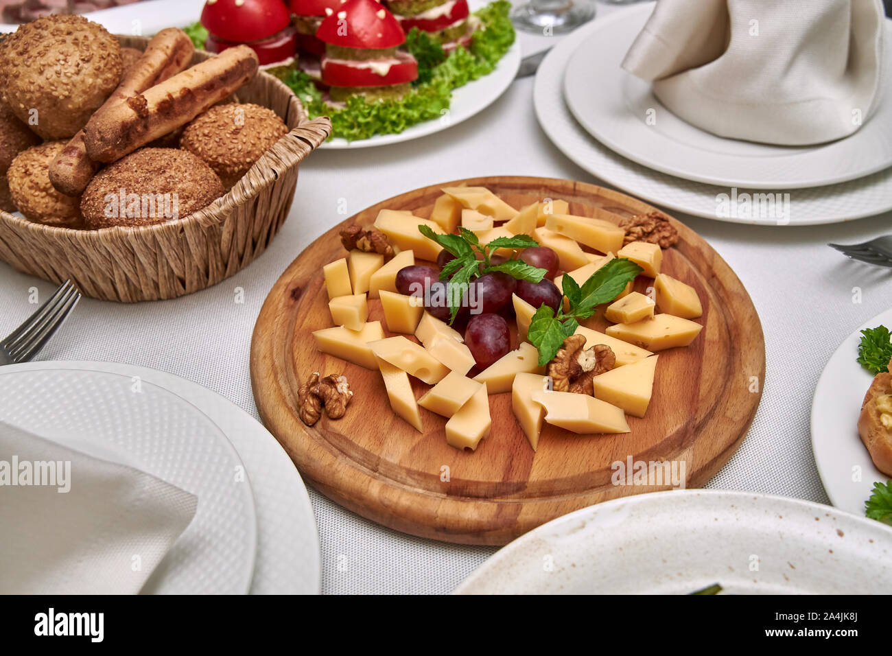 Small pieces of cheese of different varieties lie on a wooden plate on a served table in restaurant. Stock Photo