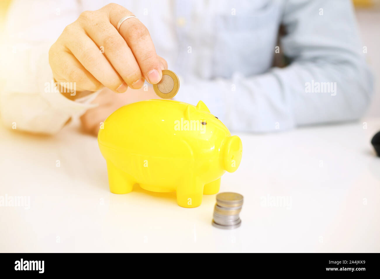 Picture of person depositing money in a yellow piggy bank. Isolated on background. Stock Photo