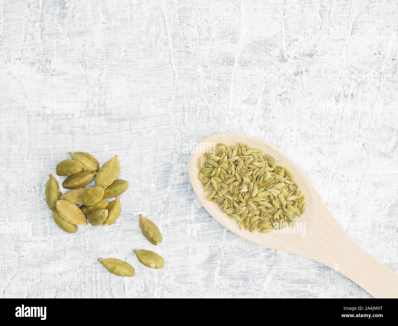 Spices and herbs help maintain good health and improve appetite, top view on white concrete background. Fennel in wooden spoon, green cardamom. Modern Stock Photo