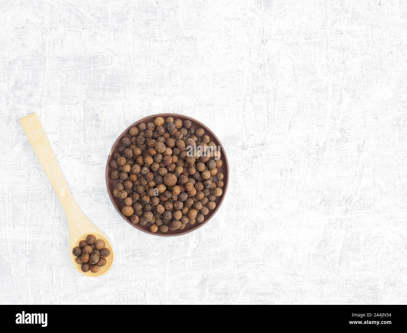 Spices and herbs help maintain good health and improve appetite, top view on white concrete background. Allspice in clay plate and in wooden spoon. Mo Stock Photo