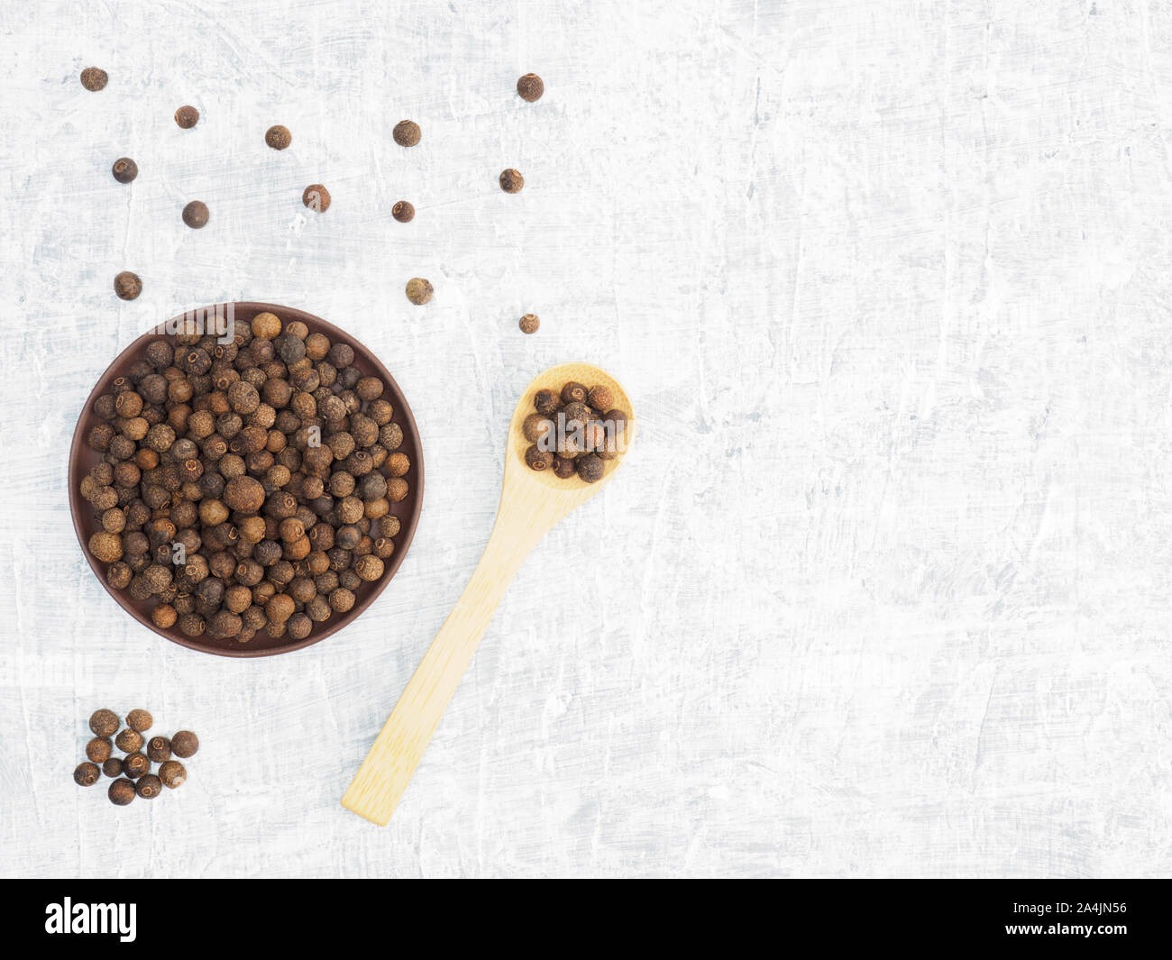 Spices and herbs help maintain good health and improve appetite, top view on white concrete background. Allspice in clay plate and in wooden spoon. Mo Stock Photo