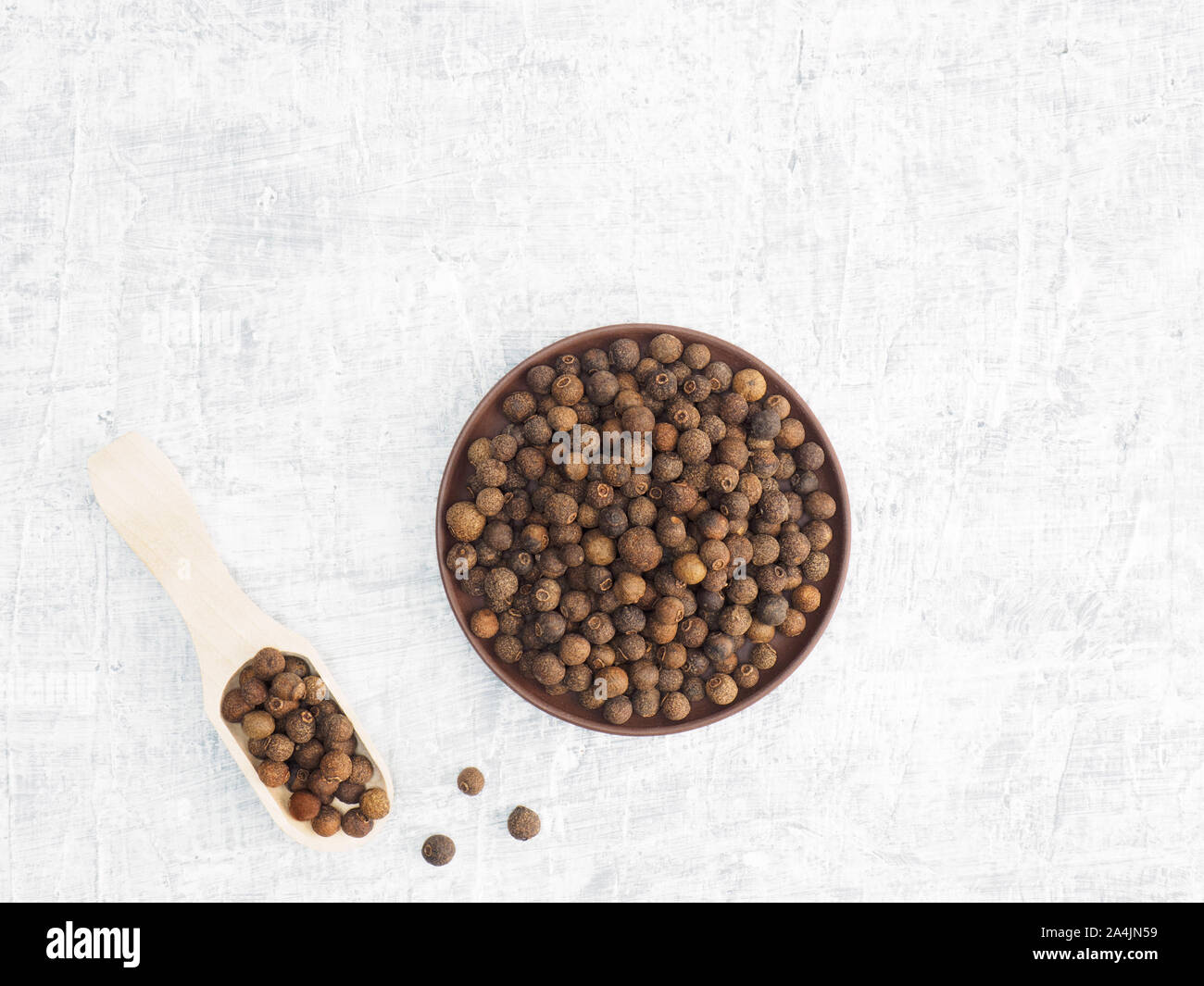 Spices and herbs help maintain good health and improve appetite, top view on white concrete background. Allspice in clay plate and in wooden scoop. Mo Stock Photo