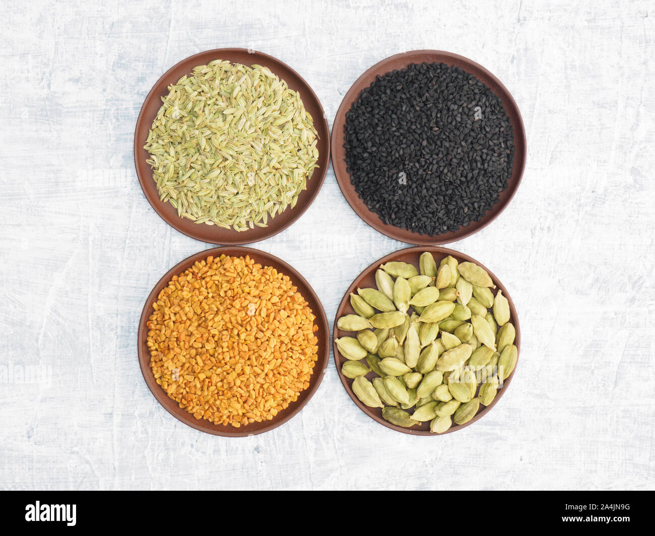 Spices and herbs set on concrete background in clay plate. Black cumin, fenugreek, fennel, green cardamom. Modern apothecary, naturopathy and ayurveda Stock Photo