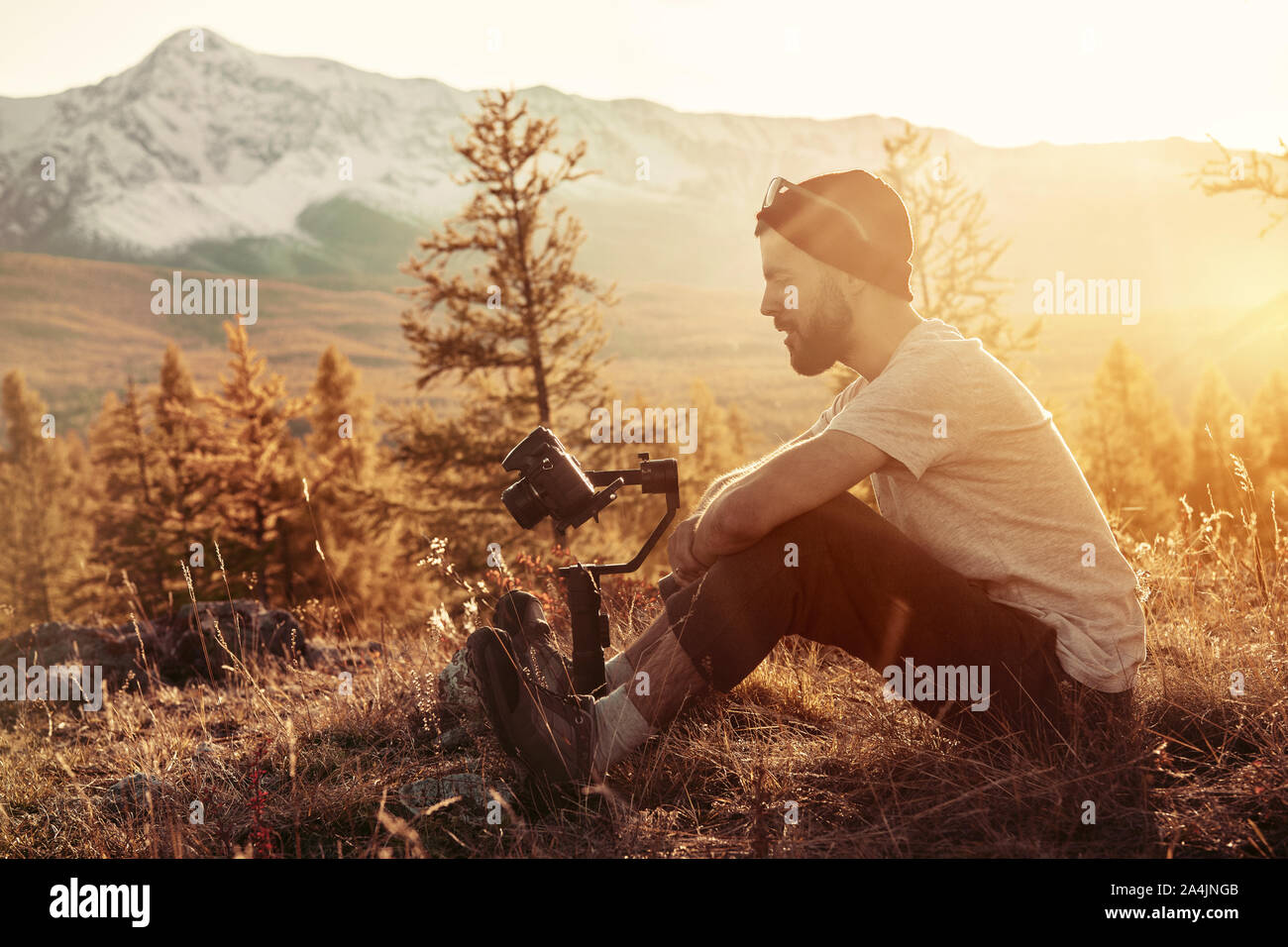 Man sits with electronic gimbal and dslr camera against mountains Stock Photo