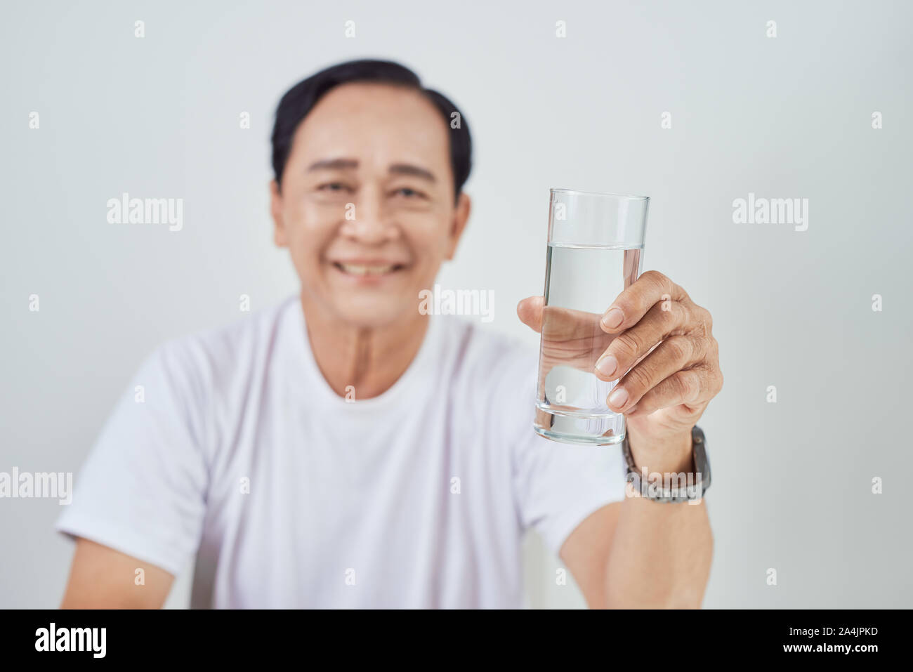 Senior man holding a glass of water and looking at the camera isolated ...