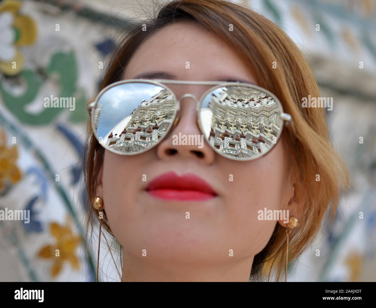 Young Chinese woman (tourist) with mirrored sunglasses looks at the faience facade of Bangkok’s famous Wat Arun temple. Stock Photo