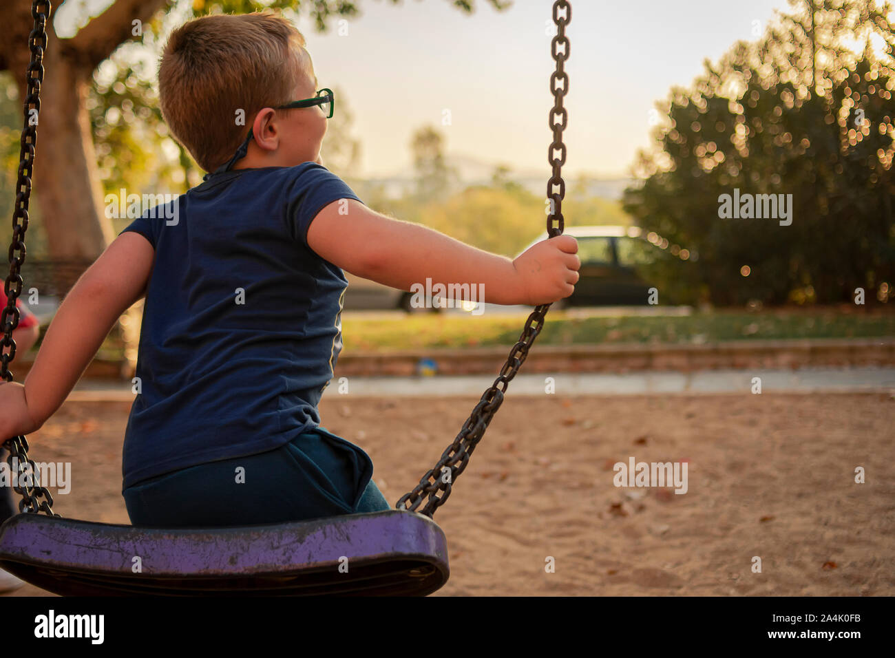 Blonde boy with his glasses swinging at the park Stock Photo