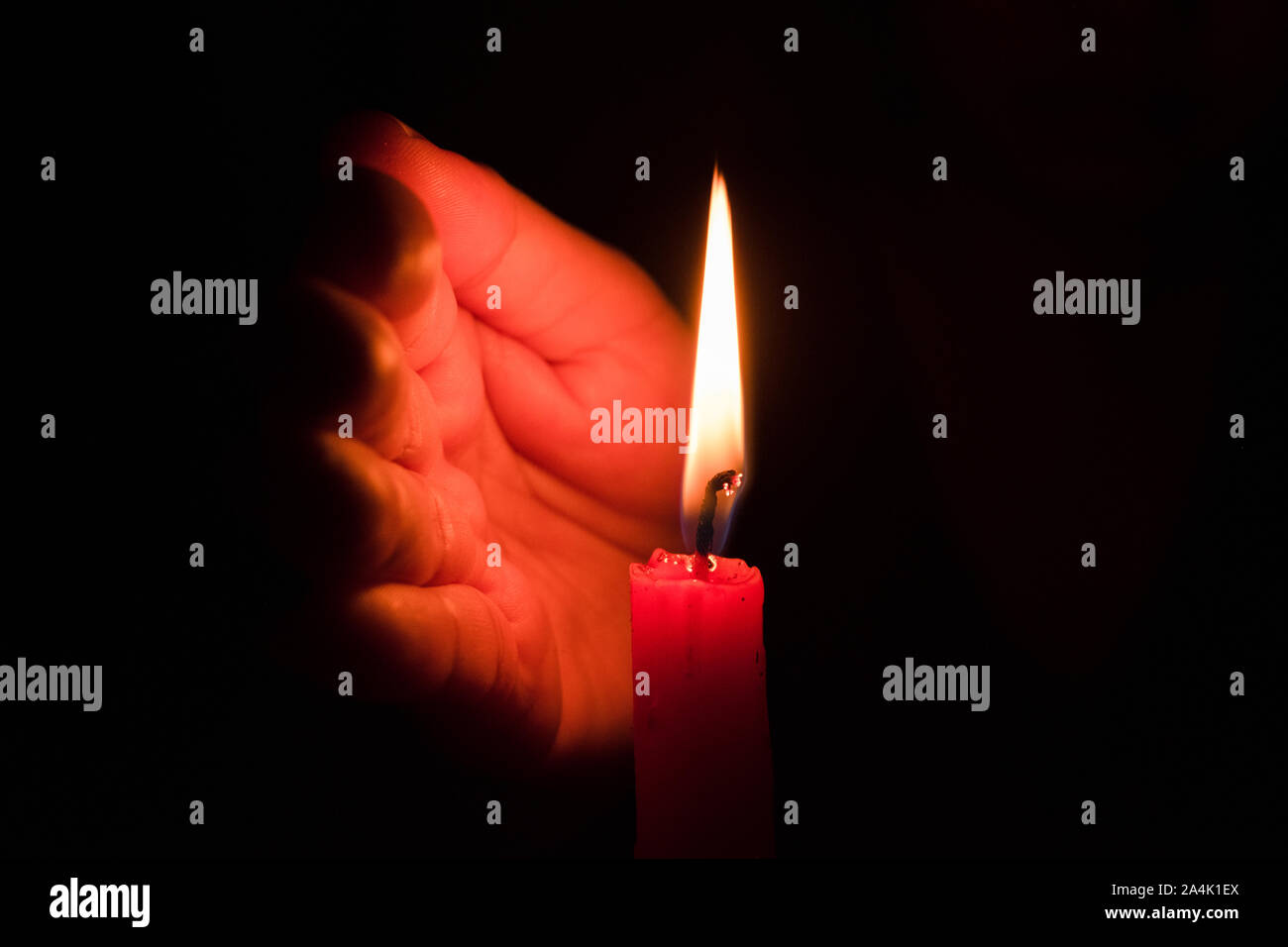 Hand protecting candle light from the wind in darkness on black