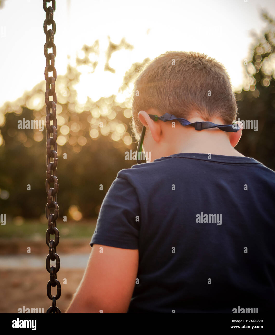 Blond boy looks sad on the floor on a park swing Stock Photo