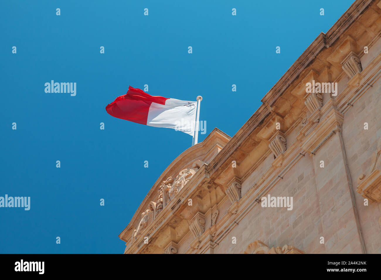 Maltese flag mounted on an old stone building waving over blue sky. Valetta, Malta Stock Photo