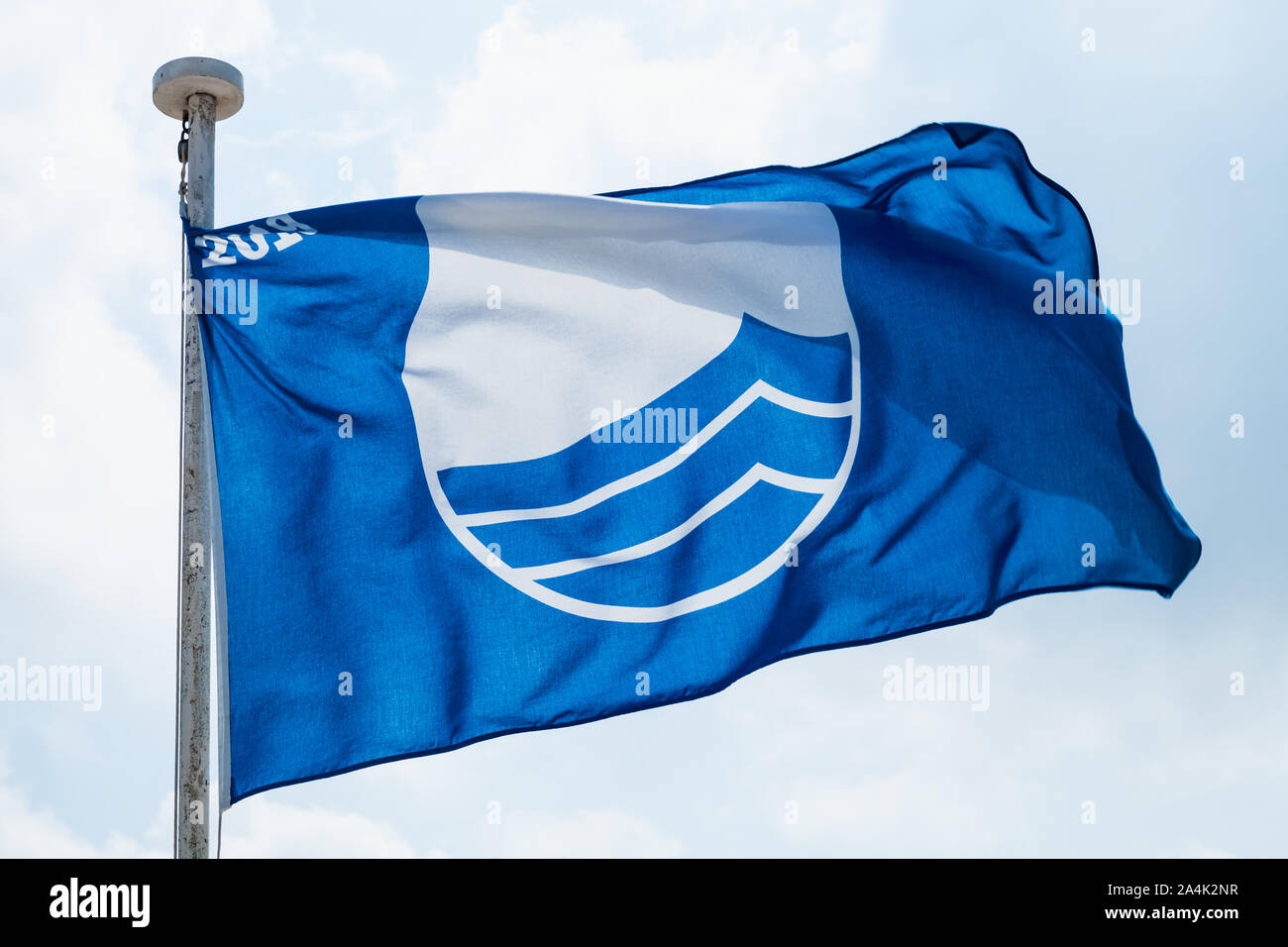 Blue Flag beach. Close up photo of the flag waving under blue cloudy sky Stock Photo