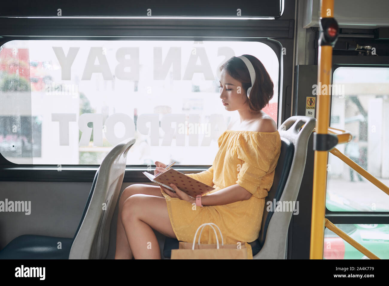 Beautiful young woman sitting in city bus and writing some notes in notebook. Stock Photo