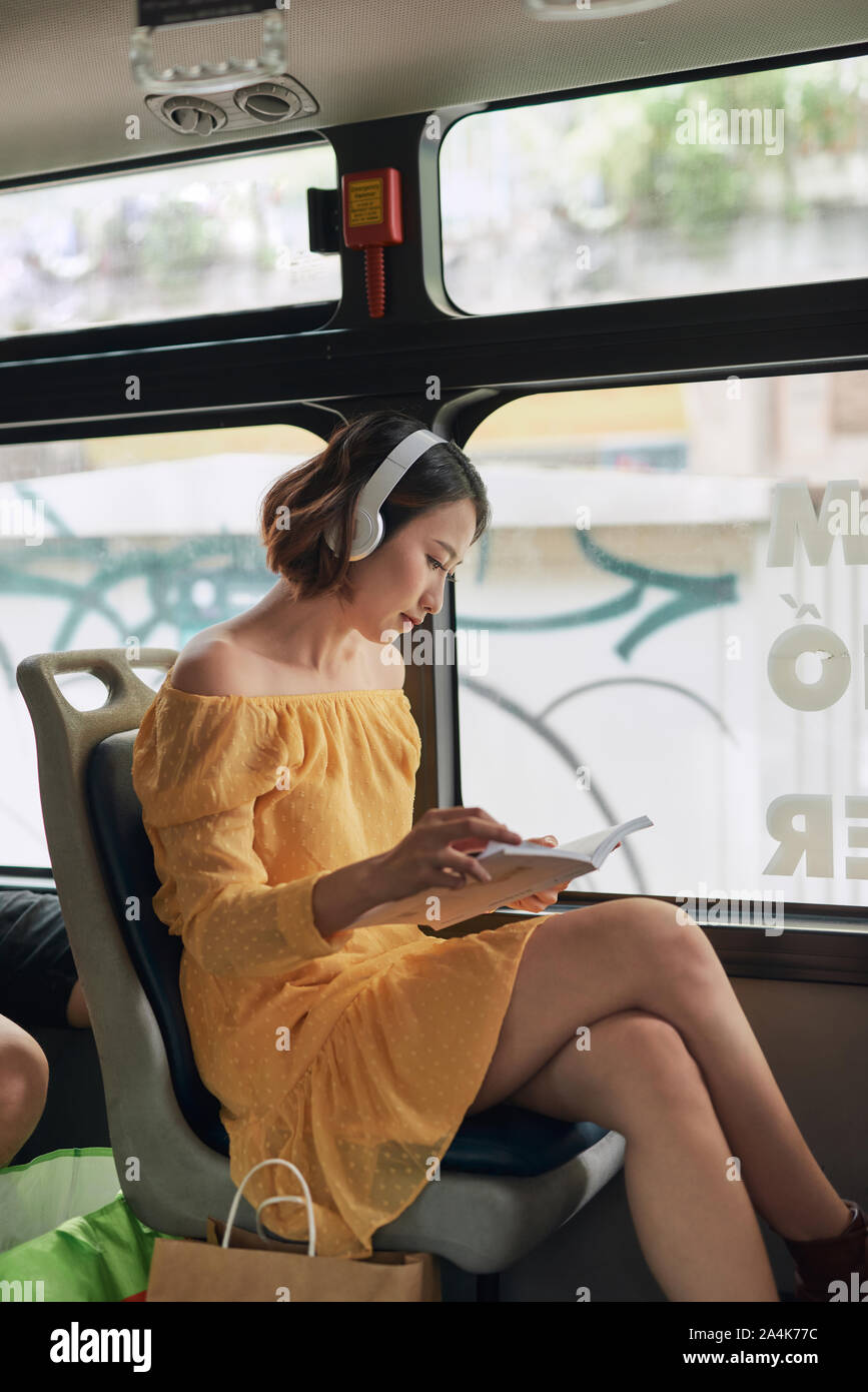 Young woman reading book while moving in the modern tram, happy passenger at the public transport Stock Photo