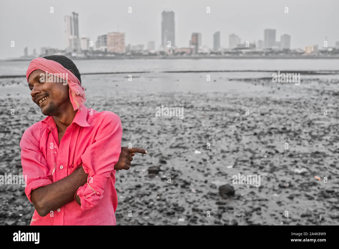 A beggar, lower left arm amputated, standing next to murky Worli Bay, near Haji Ali Mosque, Mumbai, India, pointing at the nearby muck and joking Stock Photo