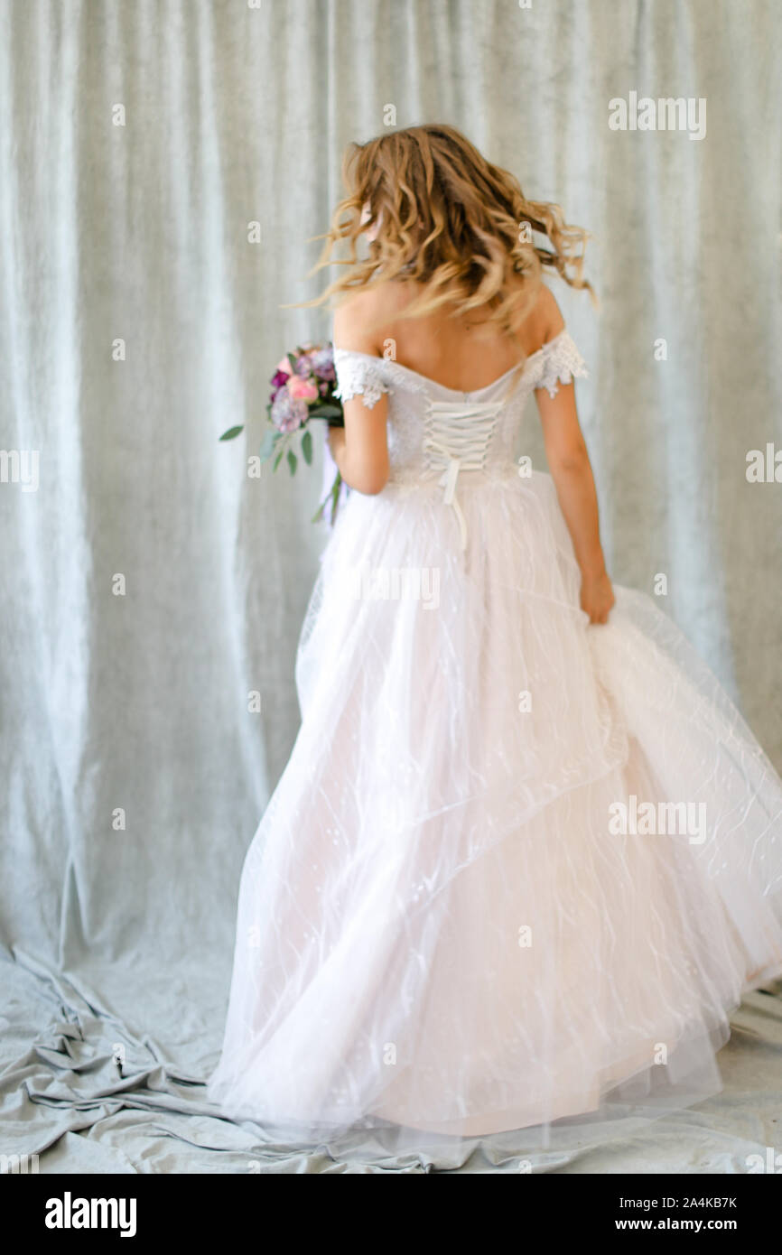 Back view of young bride standing at photo studio with flowers. Stock Photo