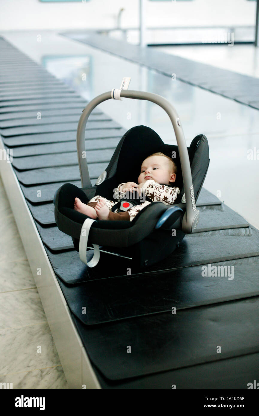 Travelling baby. Baby in car seat at baggage carousel at airport Stock