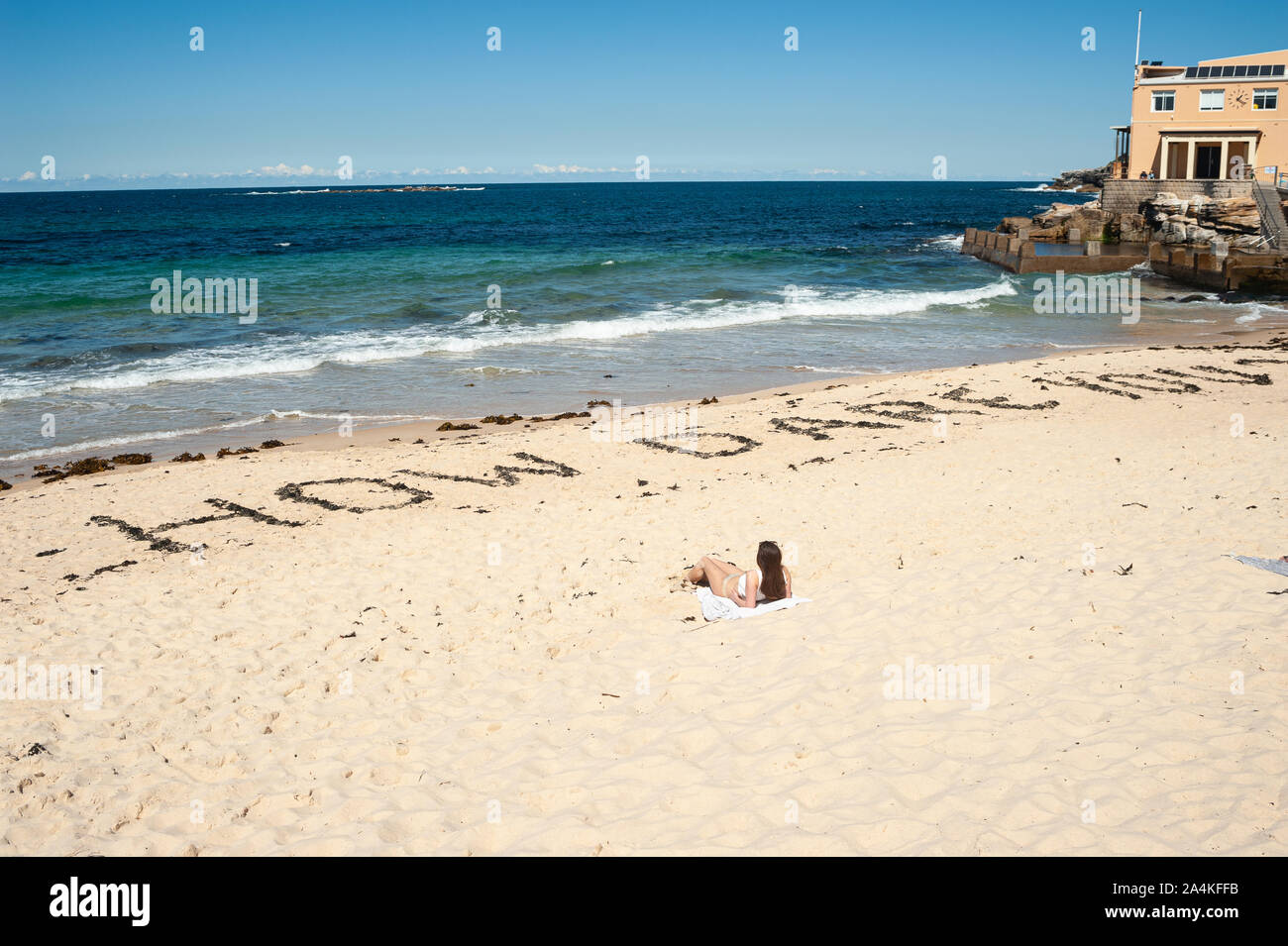 24.09.2019, Sydney, New South Wales, Australia - A woman sunbathes at Coogee Beach where the quote How Dare You? is written in the sand. Stock Photo