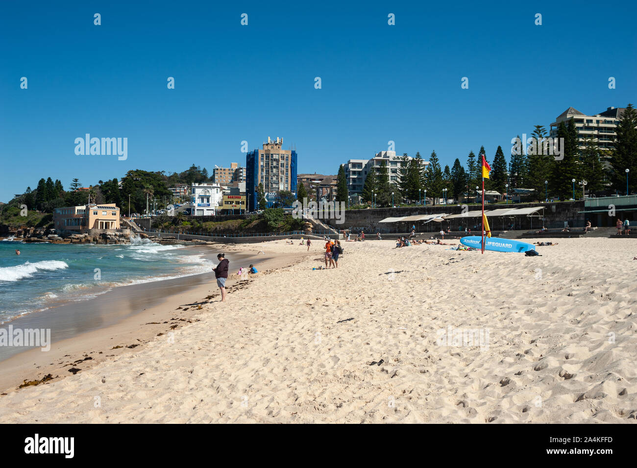 24.09.2019, Sydney, New South Wales, Australia - People in the sand under a clear blue sky on Coogee Beach with buildings in the backdrop. Stock Photo