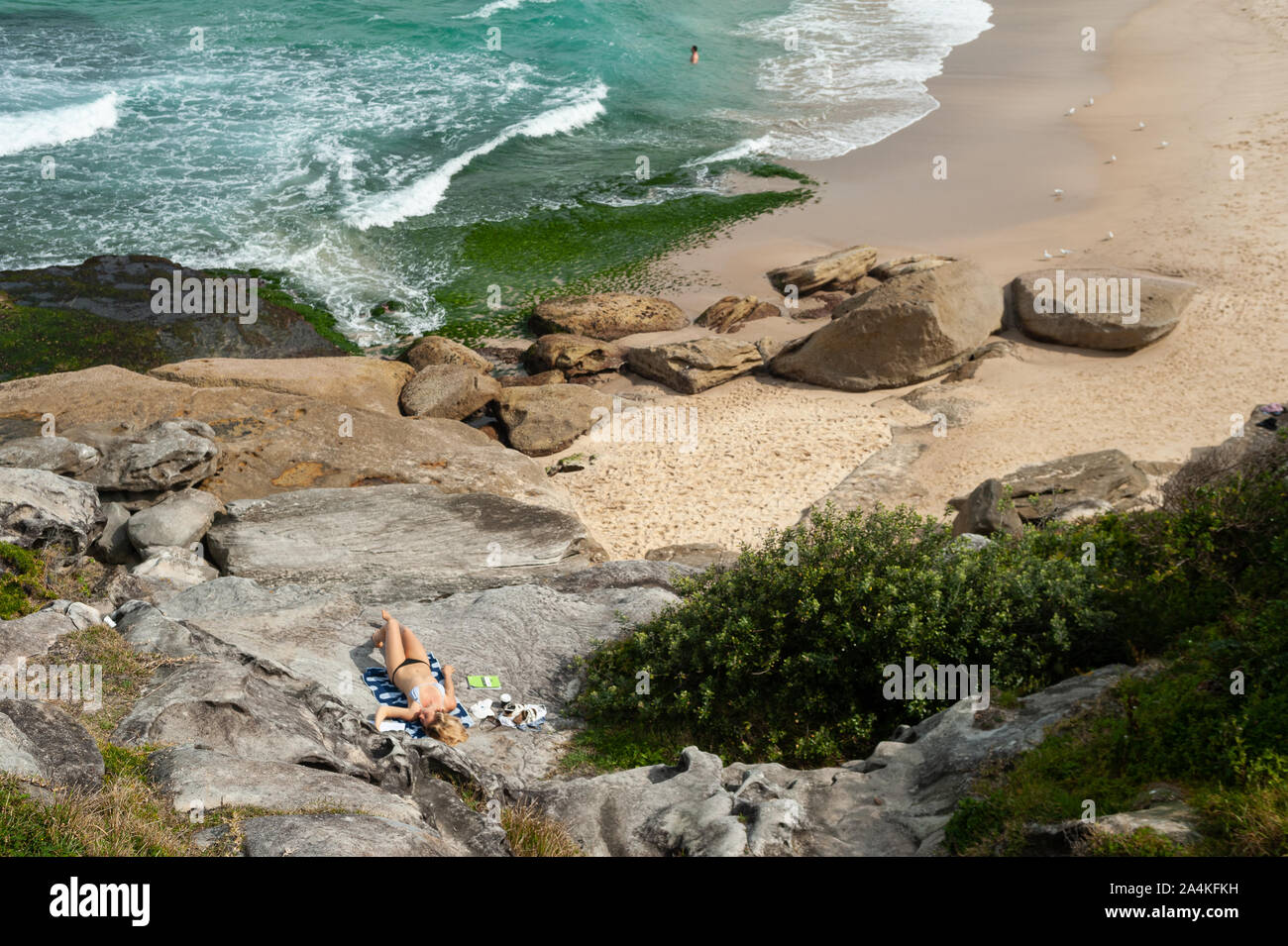 27.09.2019, Sydney, New South Wales, Australia - A woman sunbathes on the rocks at Tamarama Beach. Stock Photo