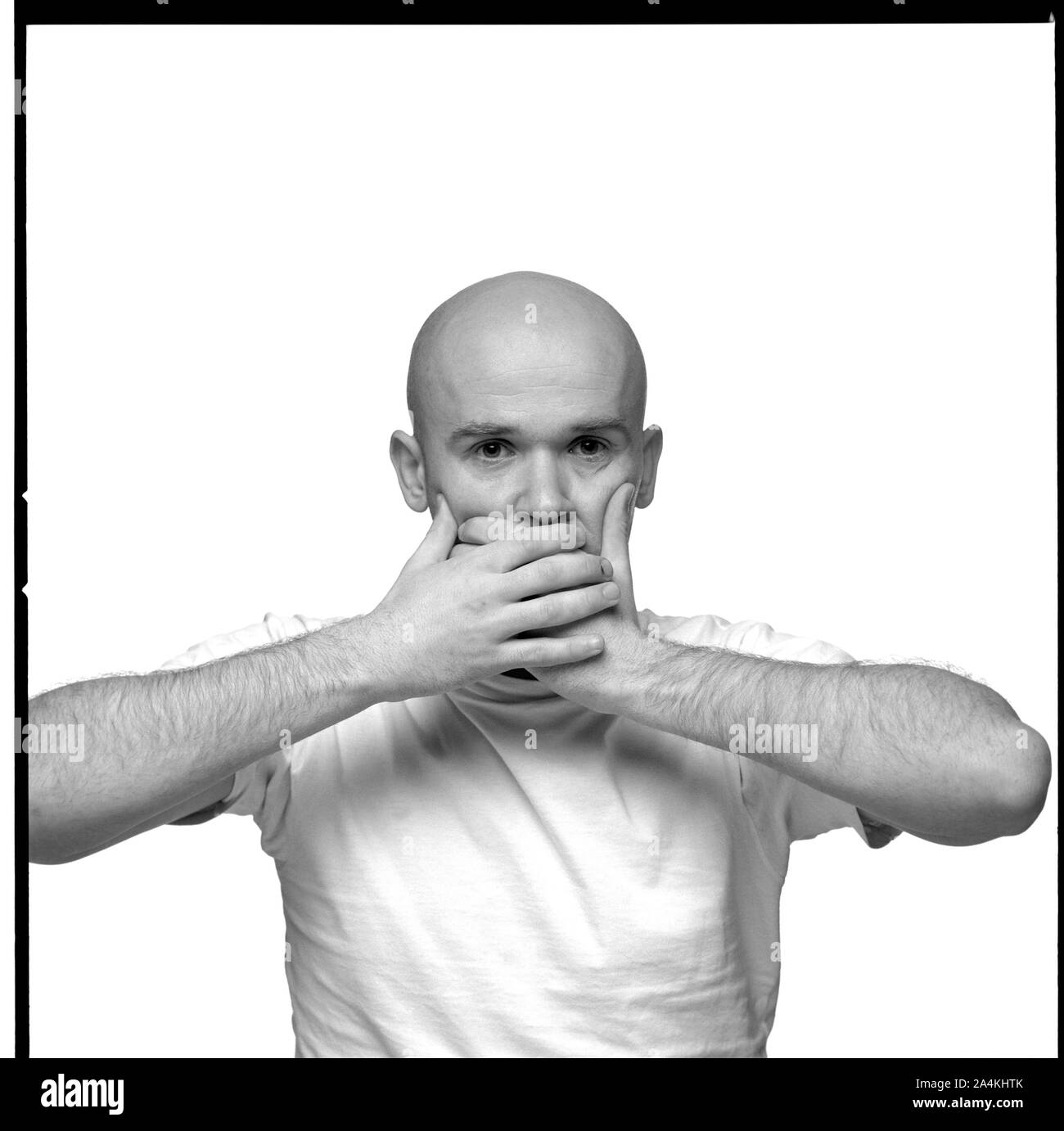 A baldheaded young man holding his hands pressed to his mouth. Stock Photo