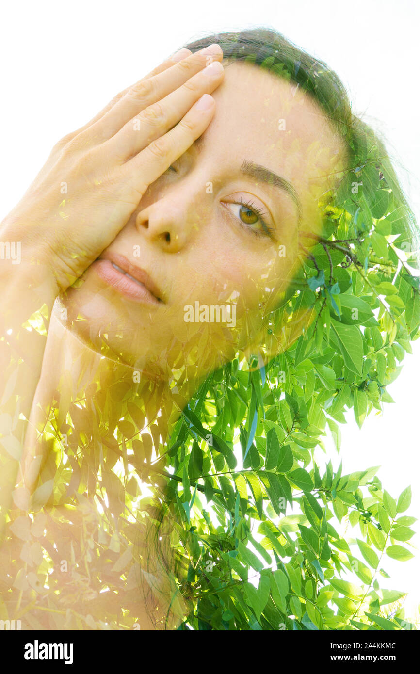 Double exposure portrait of a young, relaxed natural beauty with head tilted sideways and long brown hair combined with green tropical leaves on an is Stock Photo