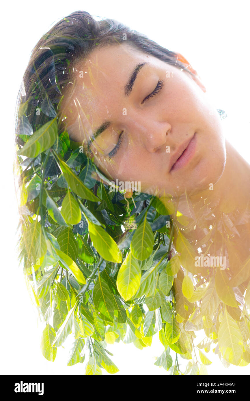 Double exposure portrait of a young, relaxed natural beauty with head tilted sideways and long brown hair combined with green tropical leaves on an is Stock Photo