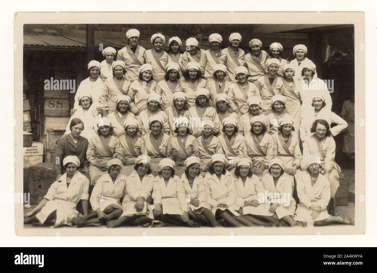 Early 1900's postcard of large group of female Mayqueen Margarine factory workers posing for a company photograph, wearing uniforms and caps,  Mayqueen Margarine printed on crate, circa 1920's, possibly Lancashire, U.K Stock Photo