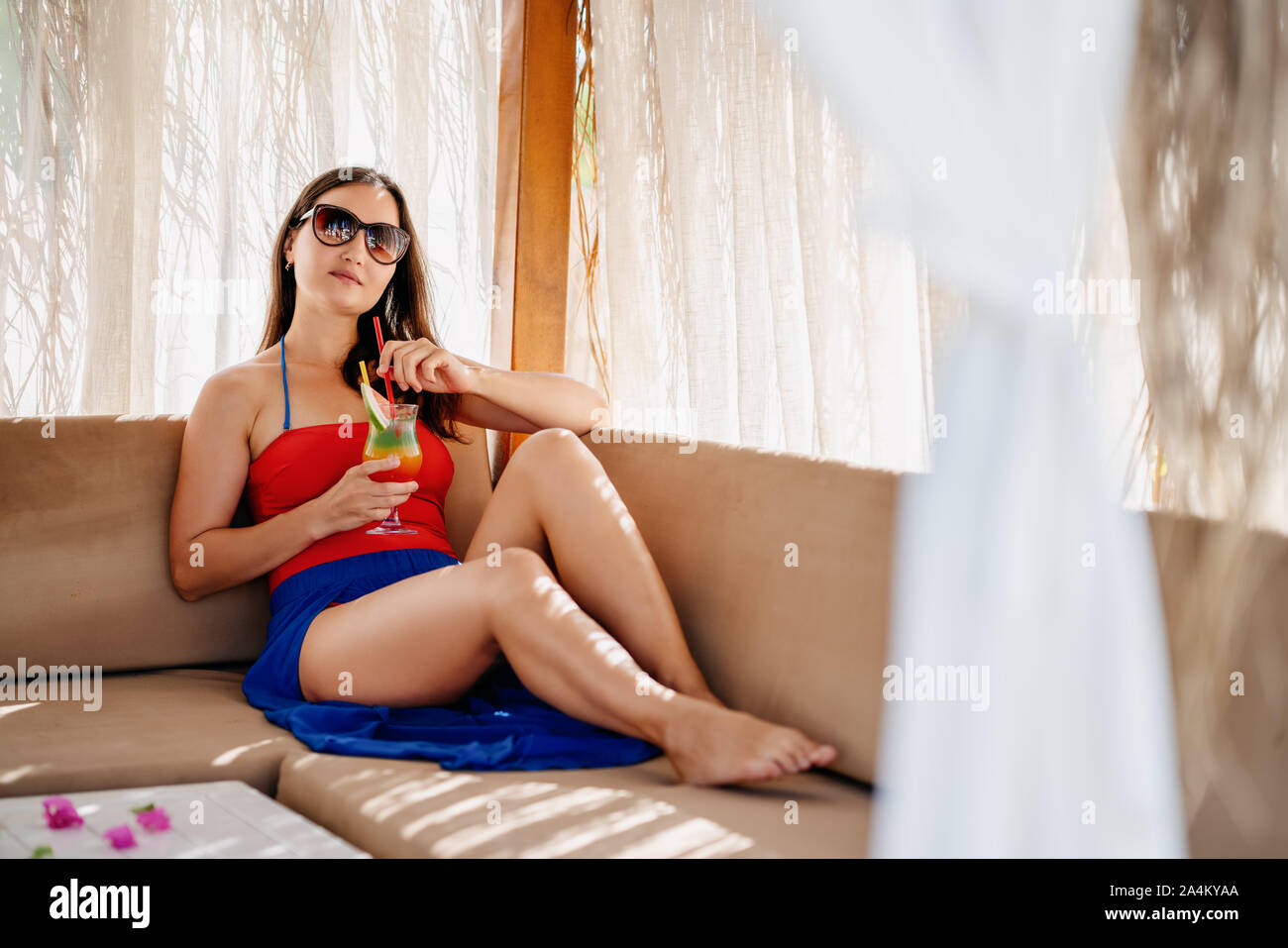 Young woman relaxing and drinking some beverage in a pergola on a vacation. Stock Photo