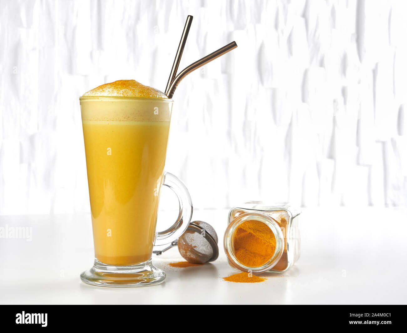 Honey sweetened turmeric latte, in a tall glass, with metal straws, on white background Stock Photo
