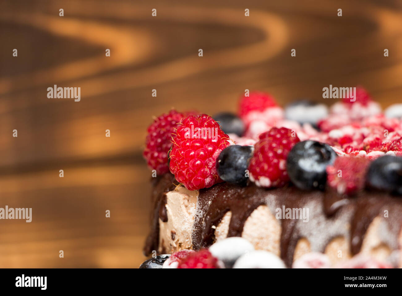 A close-up view of vegan chocolate cake covered with raspberries and blueberries, frozen in the refrigerator, on a table with blurred background. Copy Stock Photo