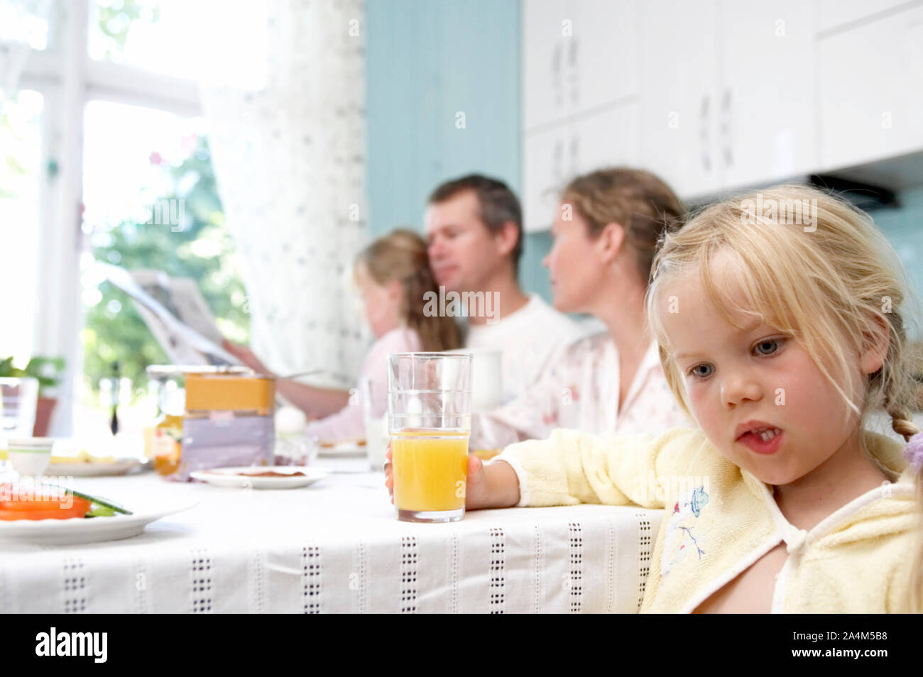 Family breakfast - little thoughtful girl drinking orange juice. Stock Photo