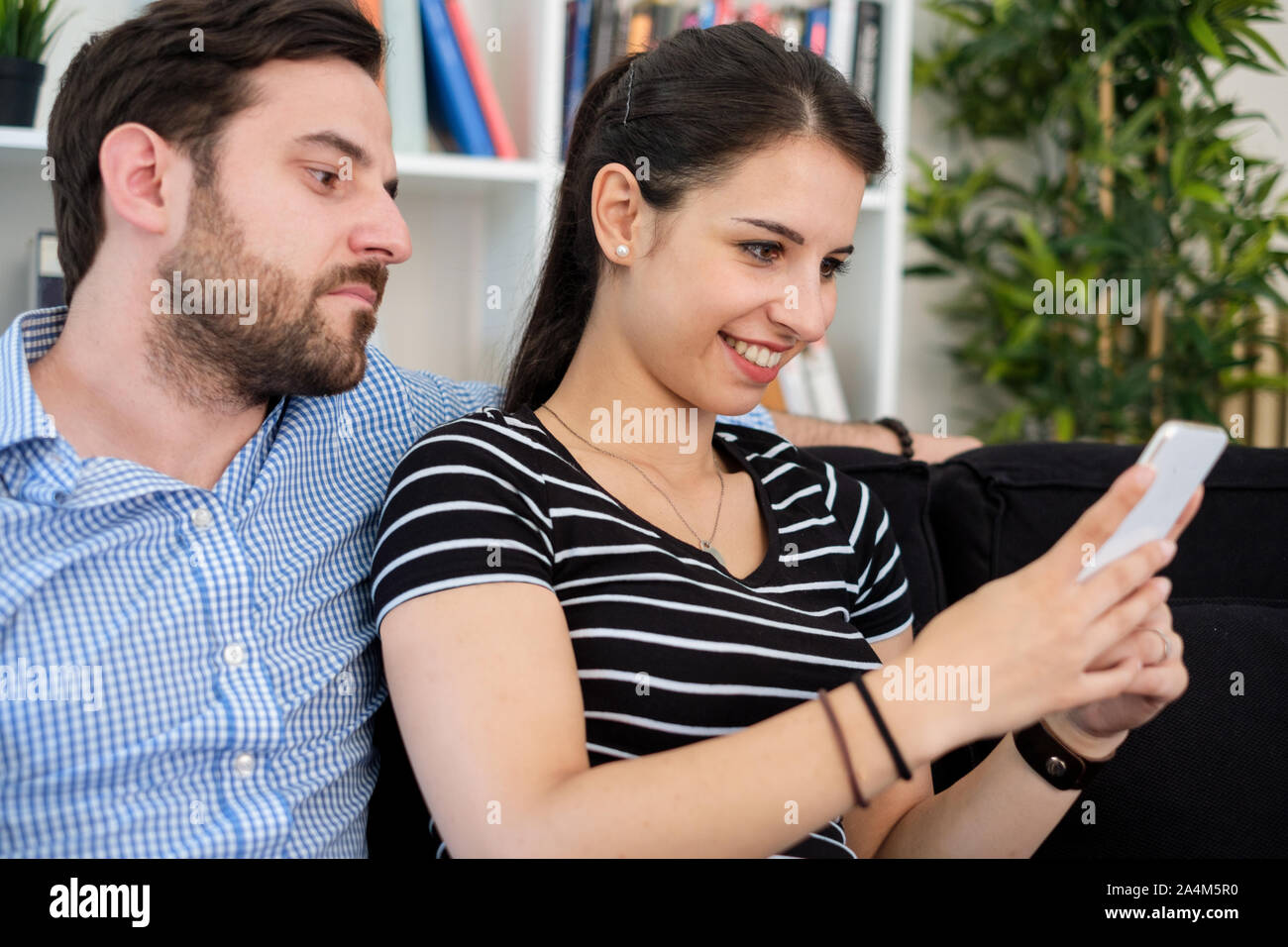 Jealous man spying girlfriend and watching her mobile phone Stock Photo