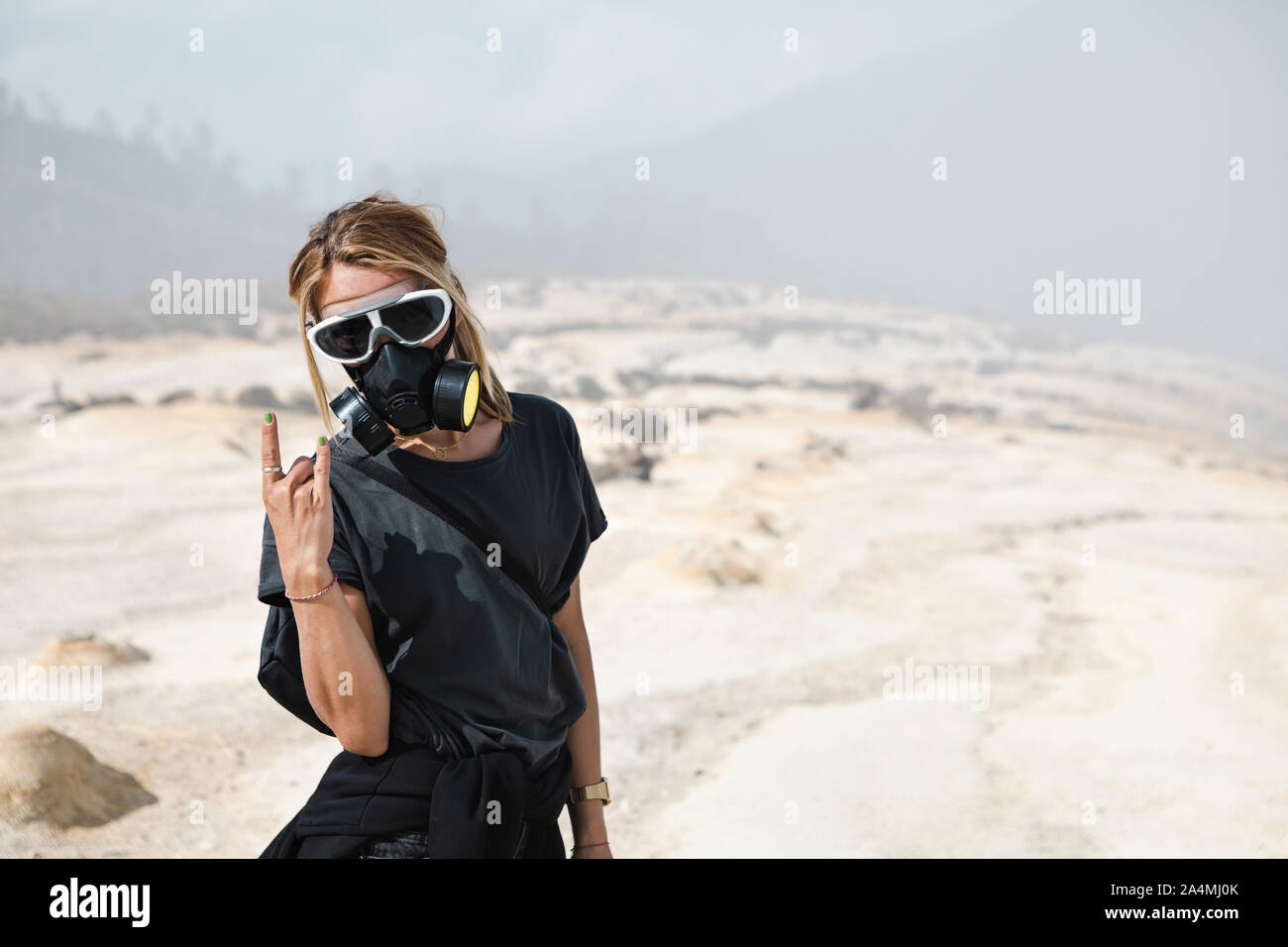 Young women in protective mask walking by wastelands around Kawah Ijen volcano crater. Post apocalypse landscape with clouds of toxic gases. Stock Photo