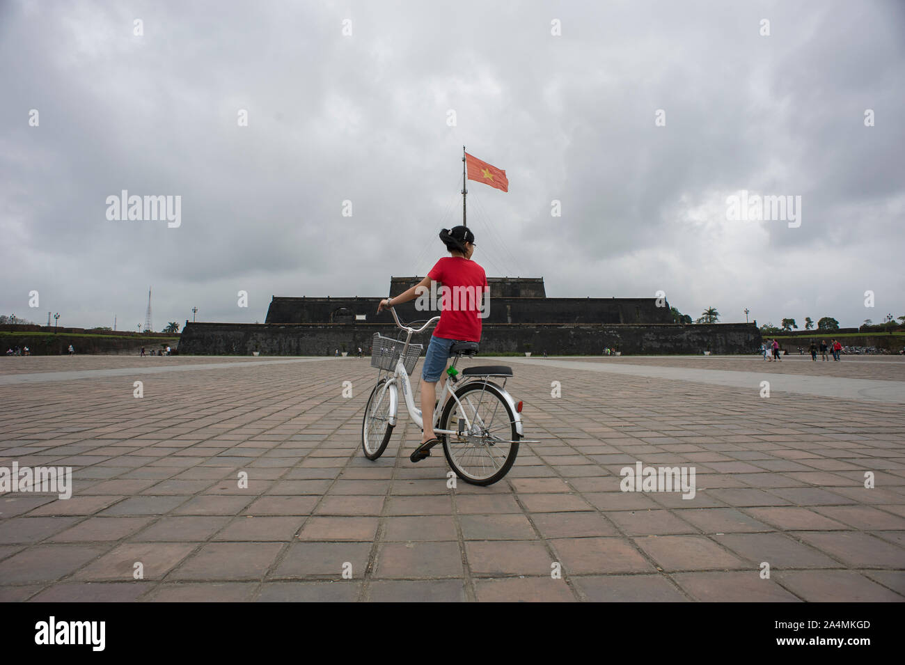 Hue, Thua Thien-Hue, Vietnam - February 27, 2011: A Vietnamese girl with red shirt cycling in a white bike in the Flag Tower (Cot Co) square Stock Photo