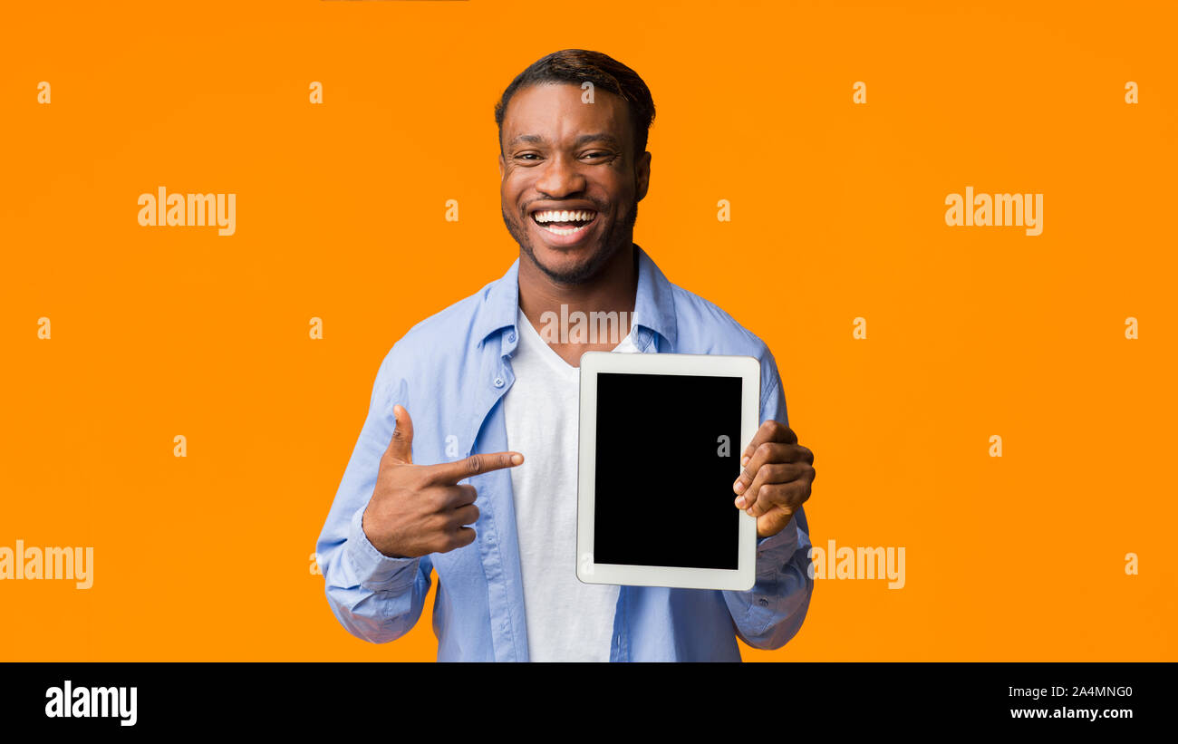 Black Guy Pointing Finger At Empty Tablet Screen, Orange Background Stock Photo