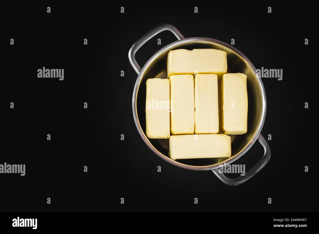 Clarification of butter, butter cubes in a steel pot on a black