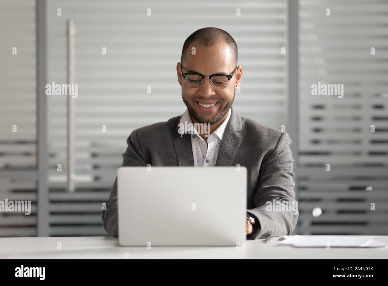 Smiling African American businessman using laptop, looking at screen Stock Photo