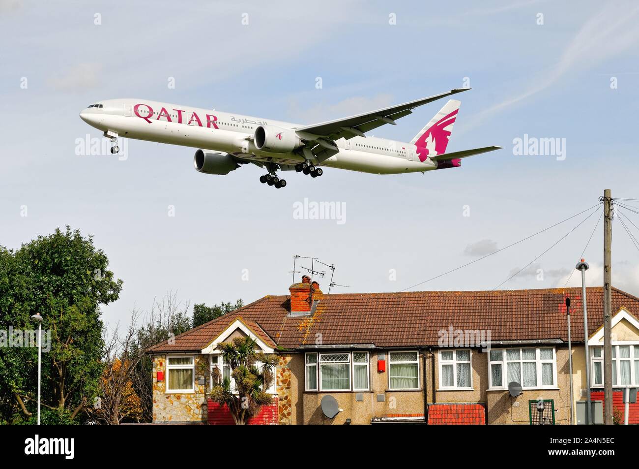 A Qatar Airways Boeing 777-300 jet flying low over rooftops at Hatton Cross on it's landing approach to Heathrow London England UK Stock Photo