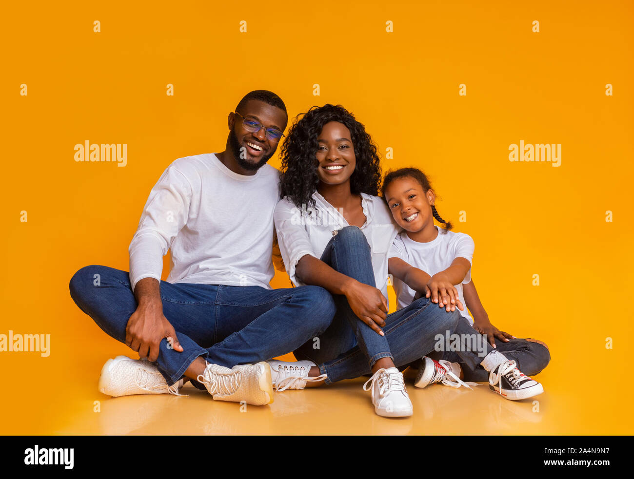 Smiling african family sitting on floor over yellow studio background ...