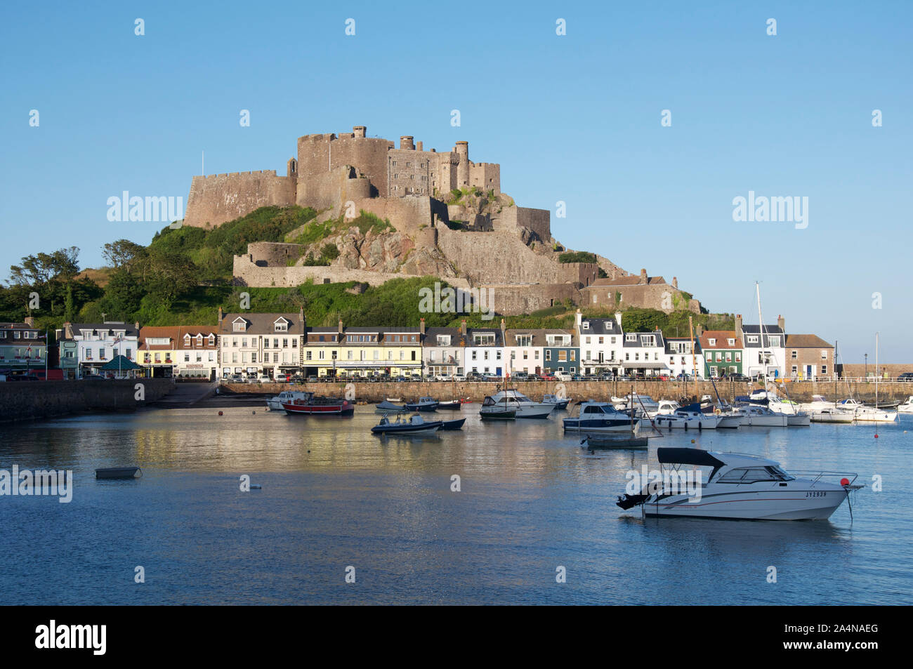 The towering historic medieval stone ramparts of Mont Orgueil Castle loom above the picturesque village and harbour of Gorey. Jersey, Channel Islands. Stock Photo