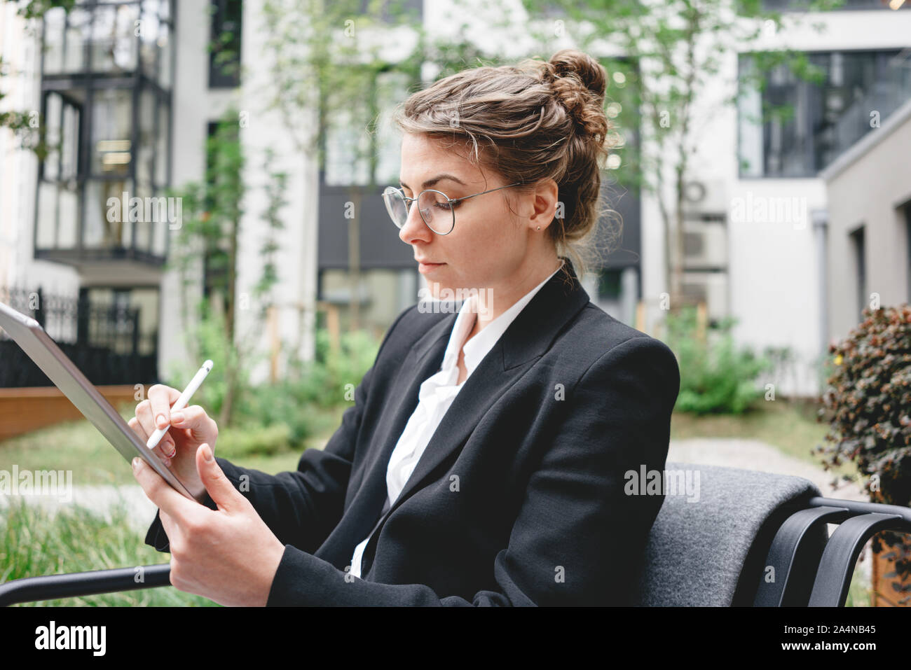Businesswoman at cafe on veranda using gadgets for digital work. Young business woman sitting at coffee shop working on digital tablet. Stock Photo