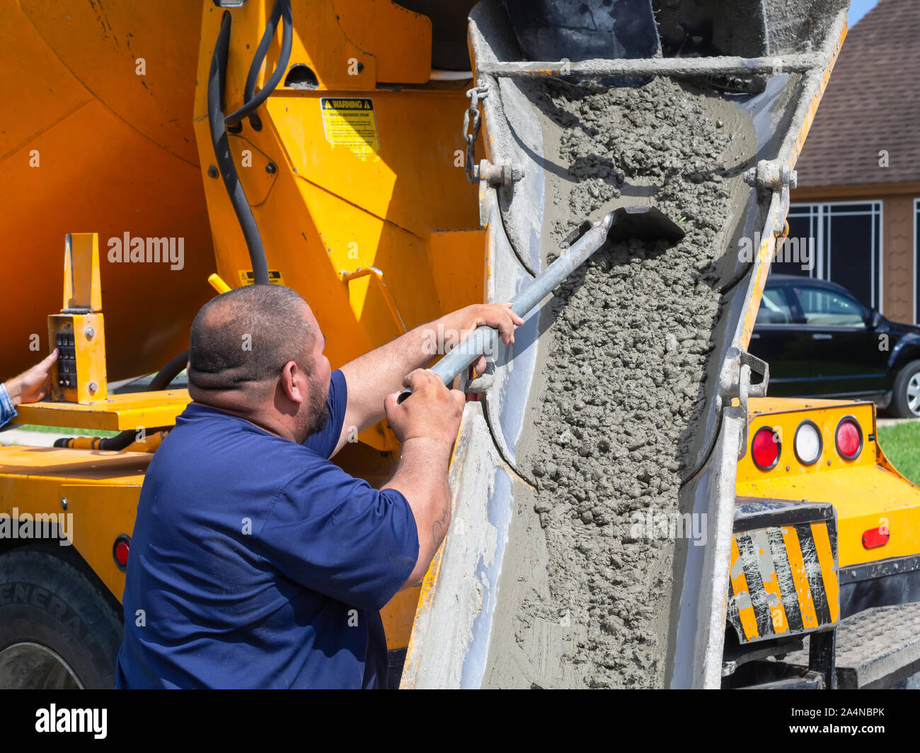 Man pulls wet concrete down chute from concrete mixing truck with a