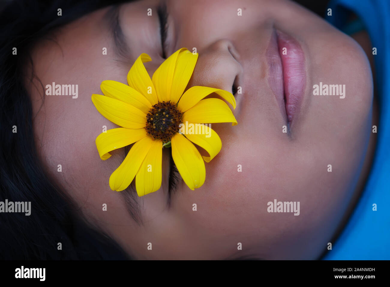 A young girl with a yellow California native flower resting on her eye while she meditates. Stock Photo