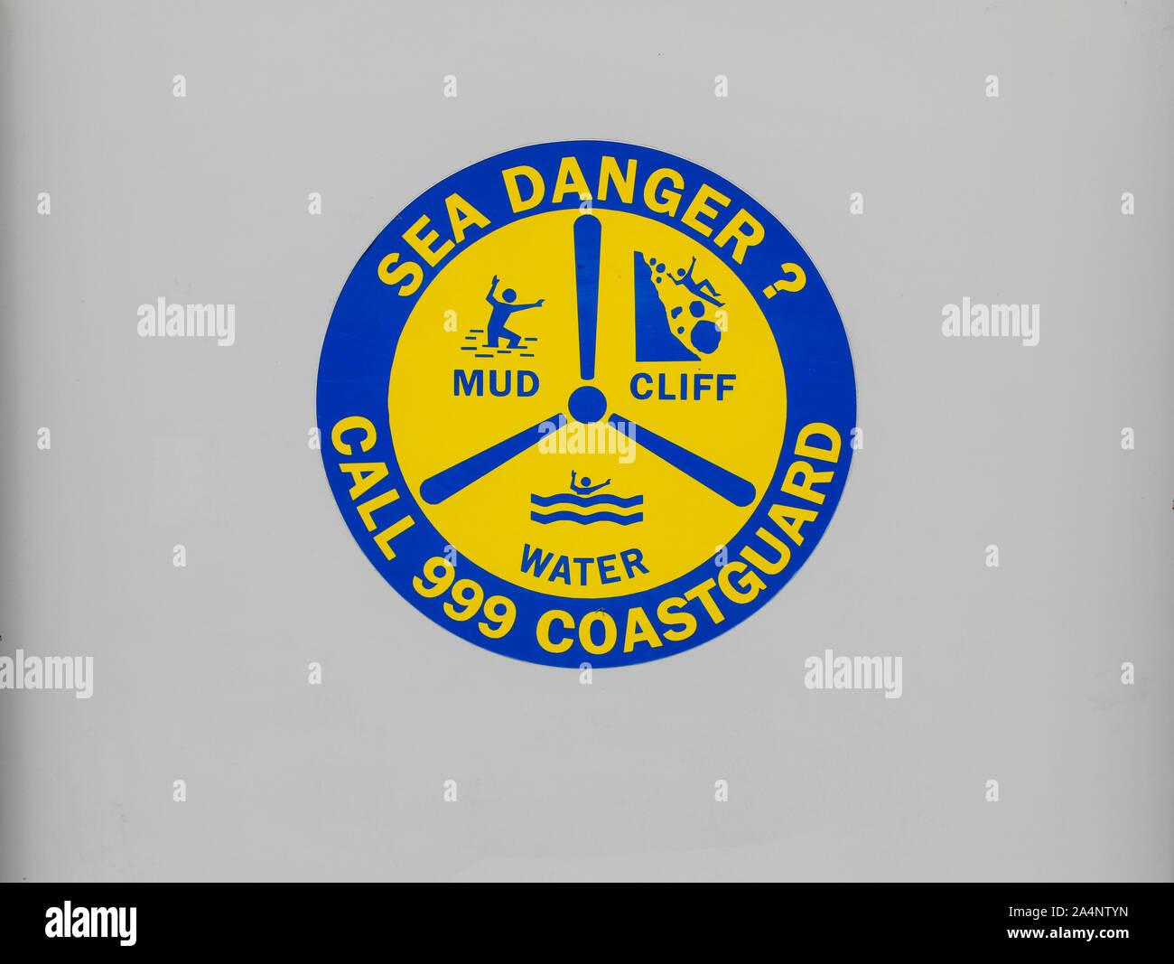 A sign saying 'Sea danger - call 999 coastguard' and mud, cliff, water, England, UK Stock Photo