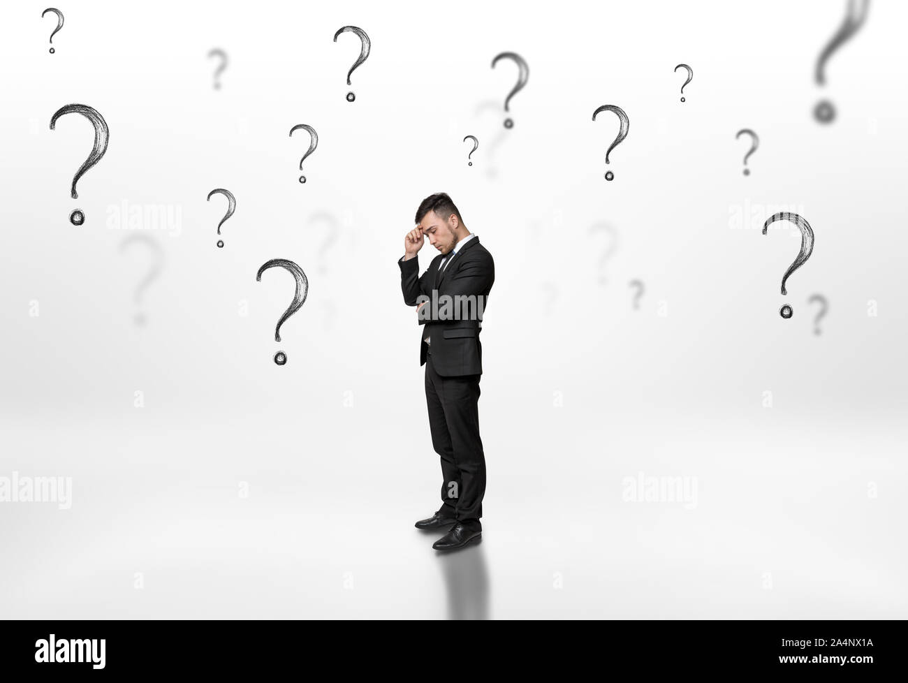 Thoughtful businessman looking upwards surrounded by question marks on white background Stock Photo