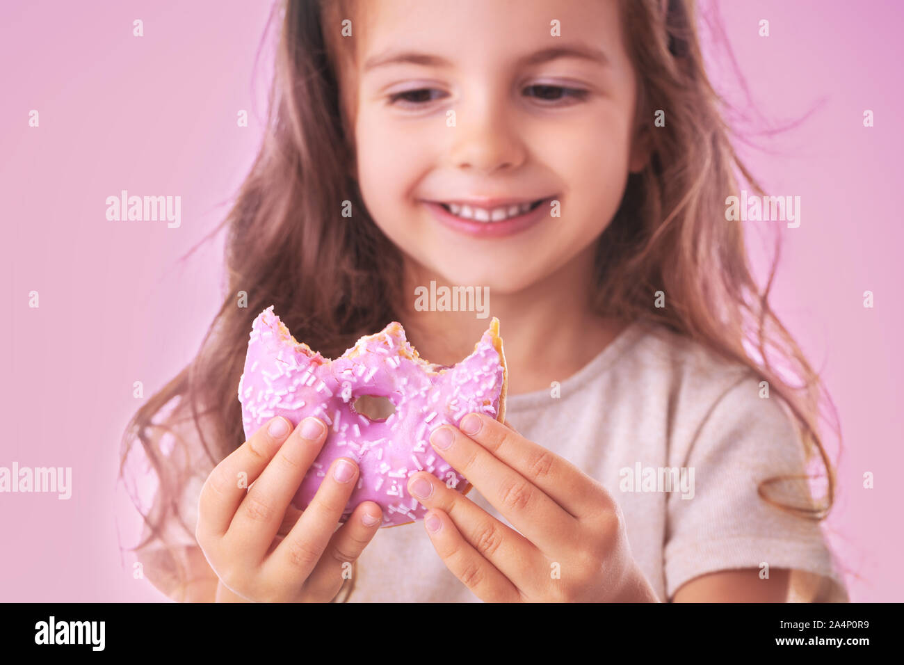 Happy little girl eating pink donut on pink background Stock Photo